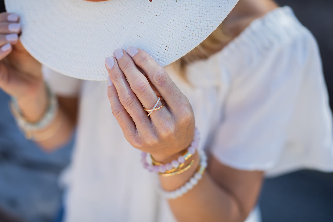 A woman wearing a hat and blonde hair, has pink finger nails and is wearing a double band ring with cubic zirconia and gold.
