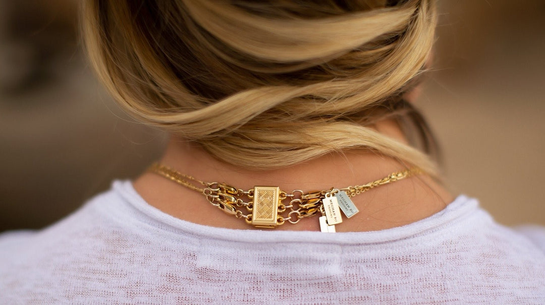 A woman with blonde hair and a white tee shirt has her hair pulled to the side and is wearing three necklaces all attached to one clasp so she doesn't have her necklaces get tangled, made by Meghan Bo Designs.