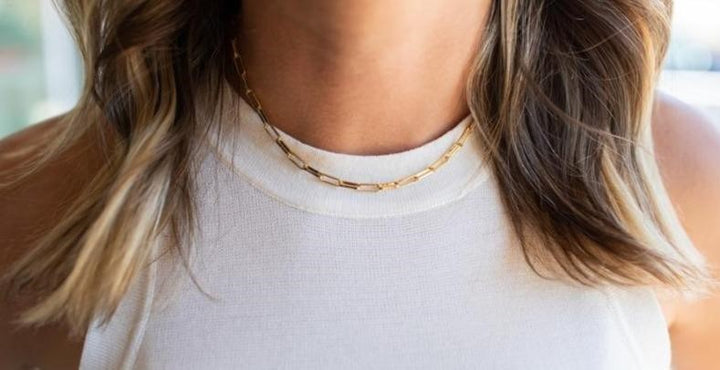 A woman with brown wavy hair is wearing a white vici collection tank top and a choker made with paperclip links made by Meghan Bo Designs.