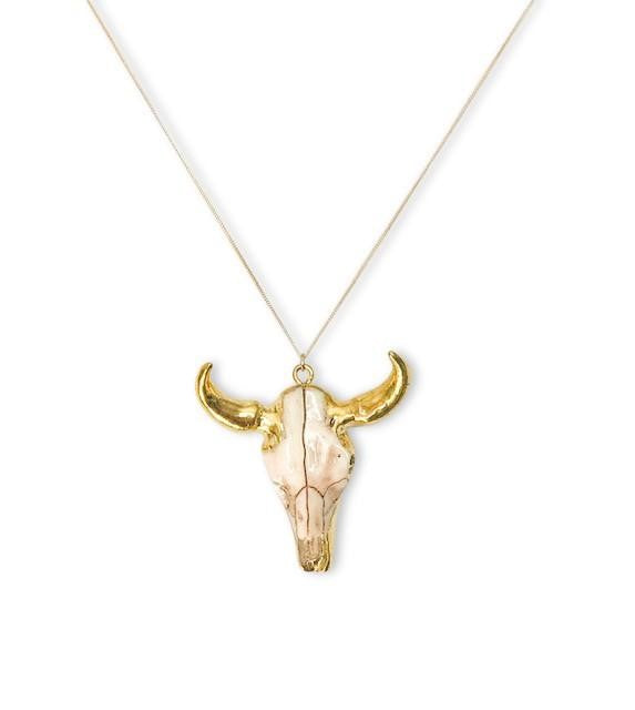 A gold chain with a bull pendant that has gold horns lays on a white surface made by Meghan BO Designs.