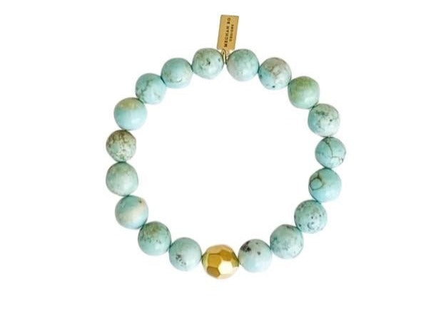 A light green beaded stretch bracelet with gold accents made by Meghan Bo Designs lays on a flat white surface.