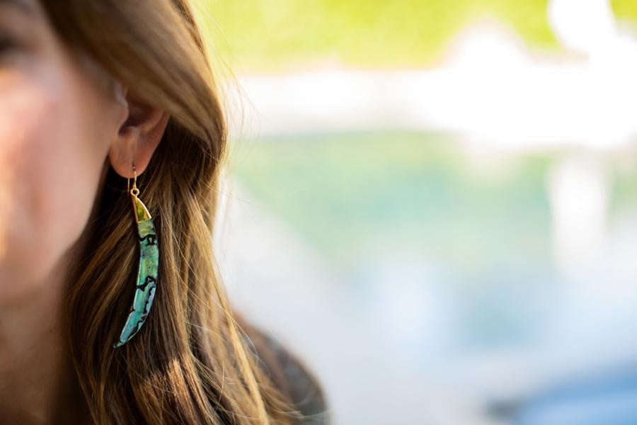 A woman with long brown hair is wearing a pair of abalone shell earrings with gold on the top and a gold ear wire made by Meghan Bo Designs.
