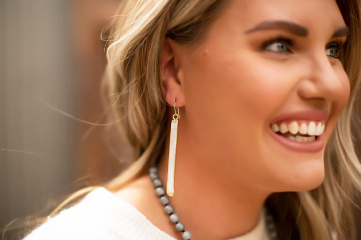 A woman with blond hair is wearing a white sweater, a silver beaded necklace and white selenite crystal dangle earrings with a gold fill ear wire made by Meghan Bo Designs.