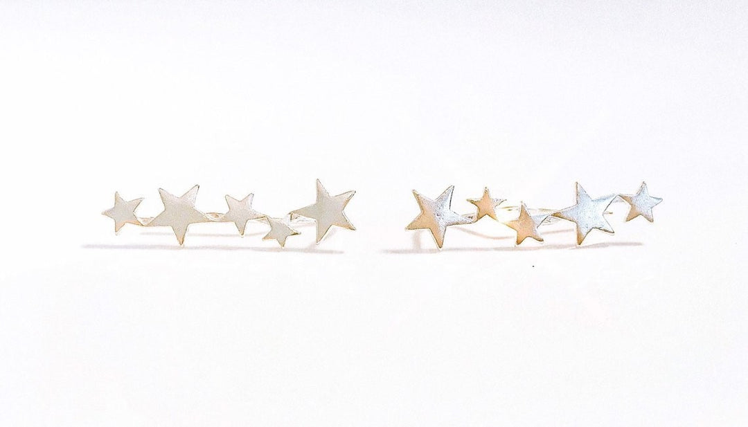 A pair of silver star ear climbers made by Meghan Bo Designs lay on a white surface.
